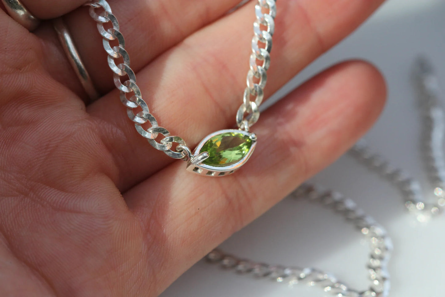 Silver necklace with a green gemstone pendant held in a hand.