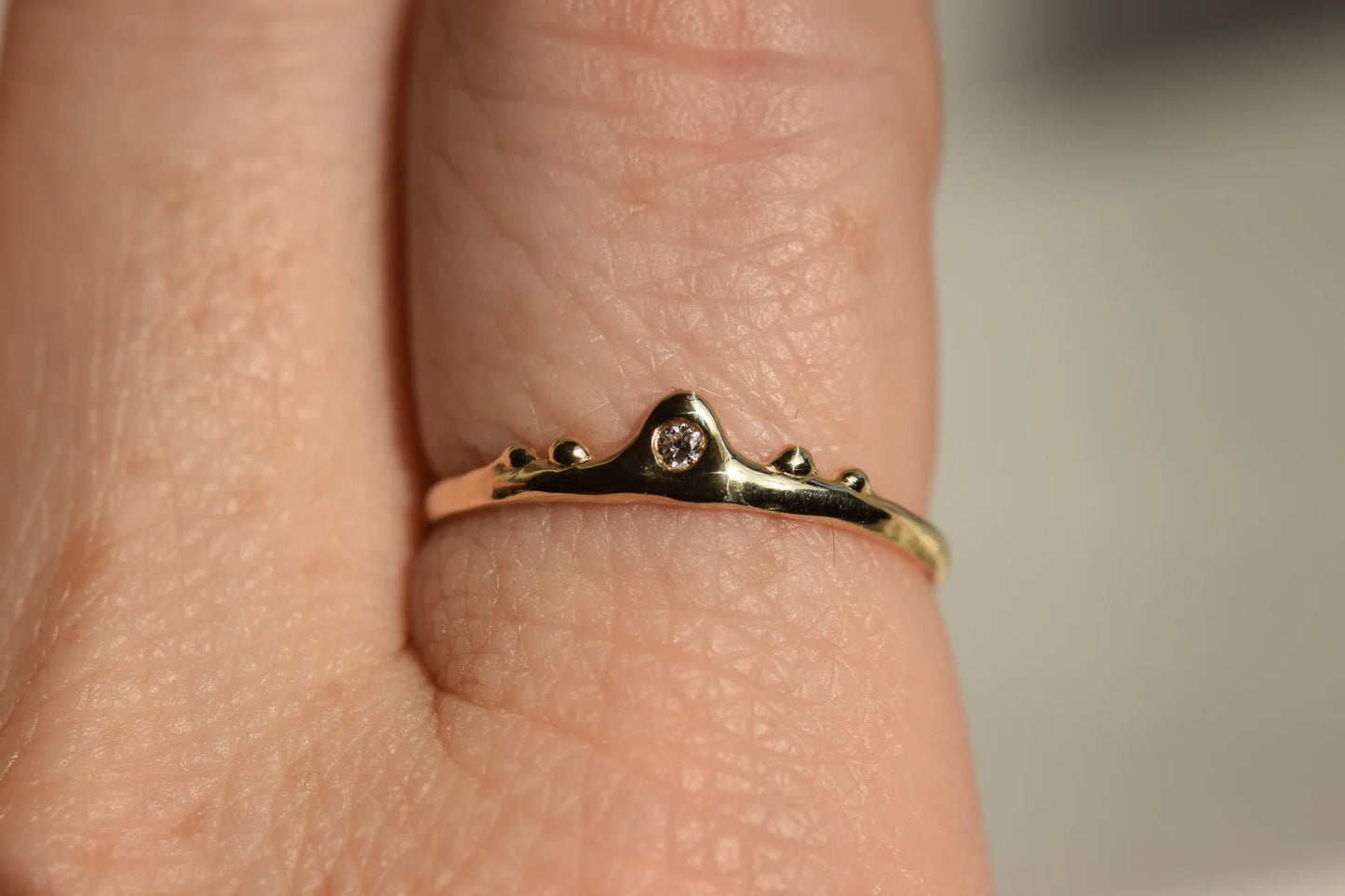 Gold ring with a diamond on a person's finger against a neutral background
