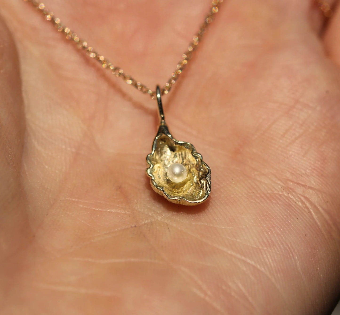 Gold pendant with a pearl on a chain held against skin