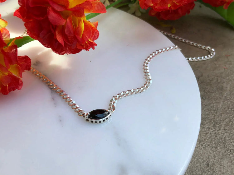 Silver necklace with a black pendant on a marble surface with red flowers in the background