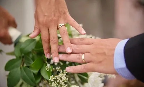Two hands with wedding rings held together in front of a floral arrangement