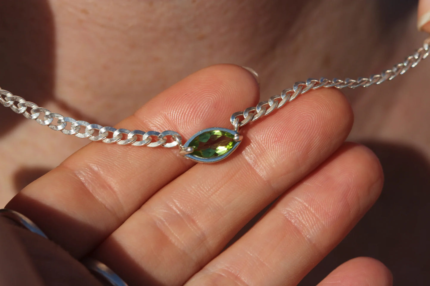 Silver chain necklace with a green gemstone on a hand