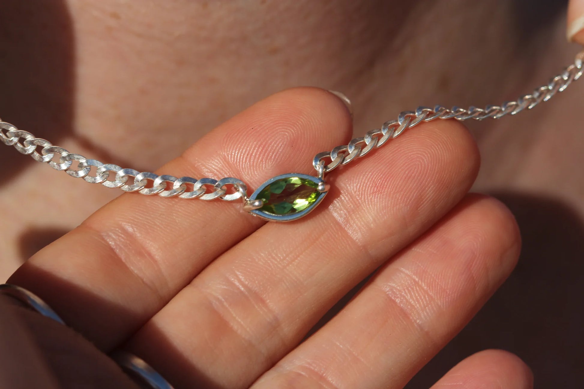 Silver chain necklace with a green gemstone on a hand
