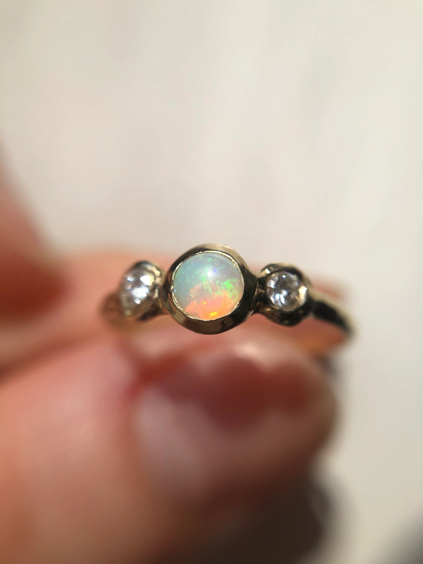 Opal ring with diamonds on a finger against a neutral background
