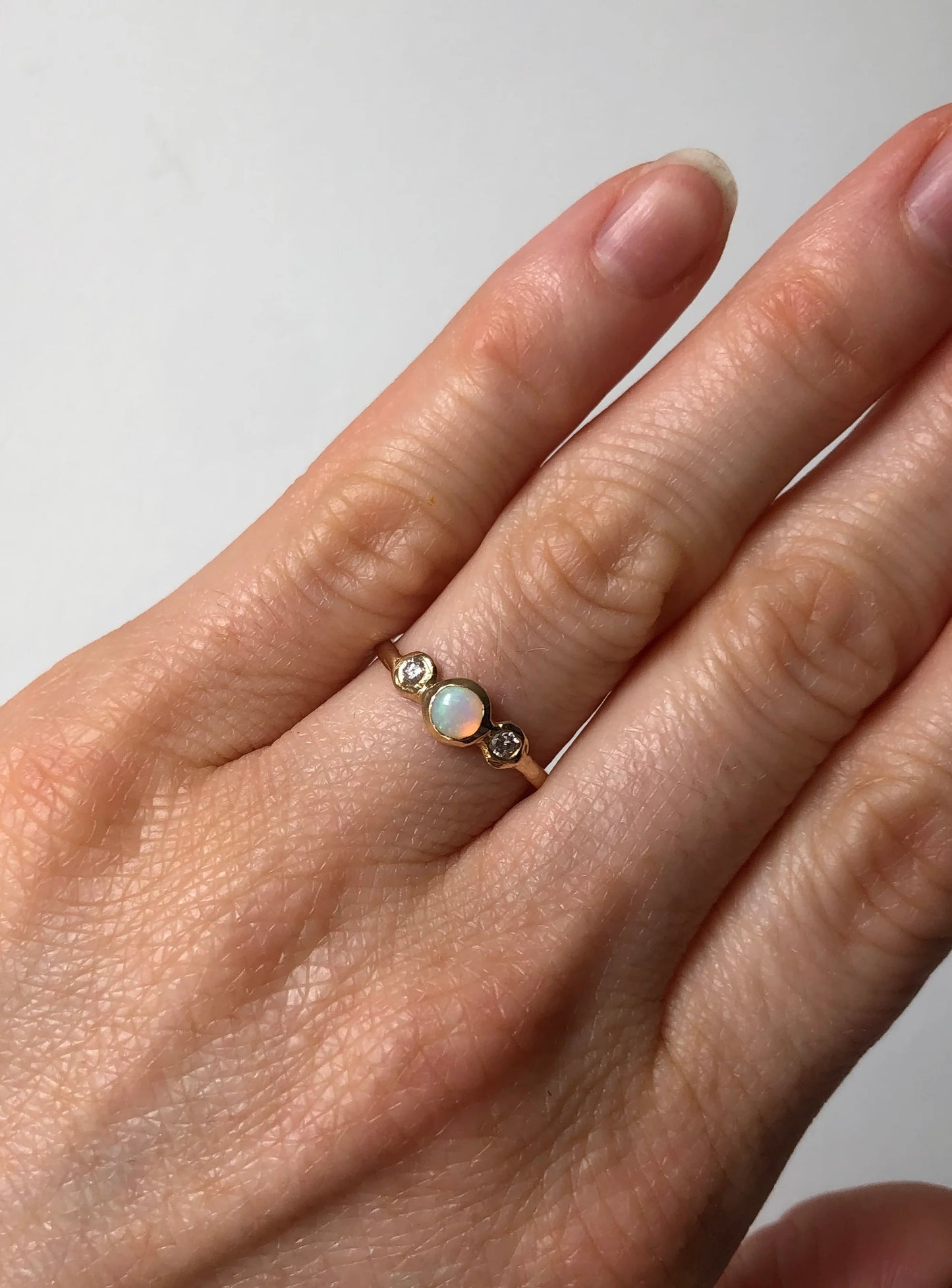 Hand wearing a gold ring with opal stones on a plain background