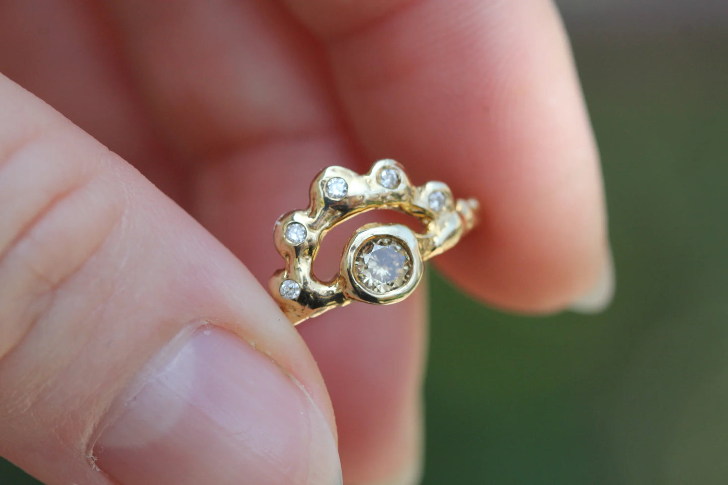 Gold ring with diamonds held between fingers against a blurred background