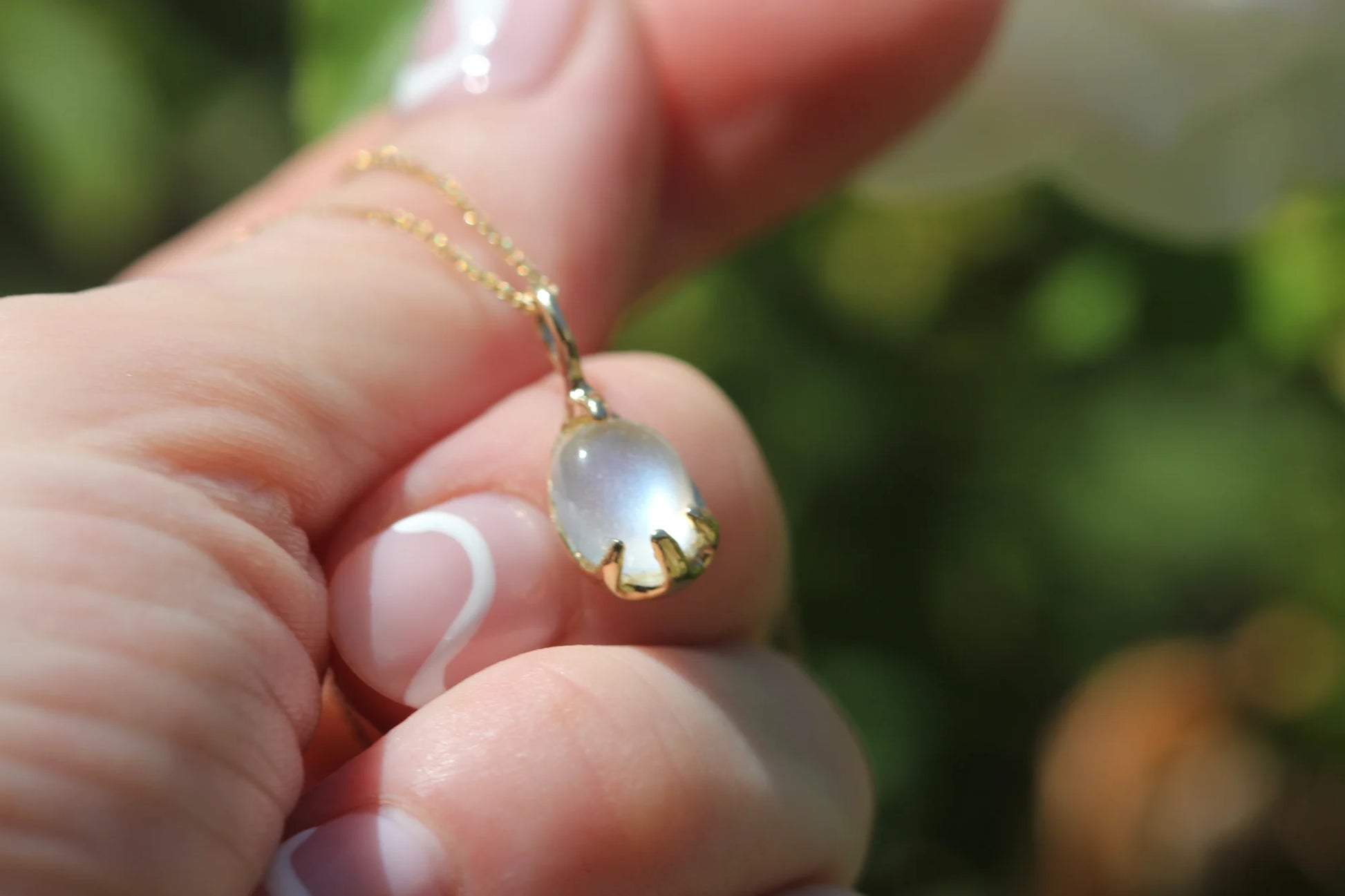 Gold necklace with a pendant held by a hand against a blurred green background