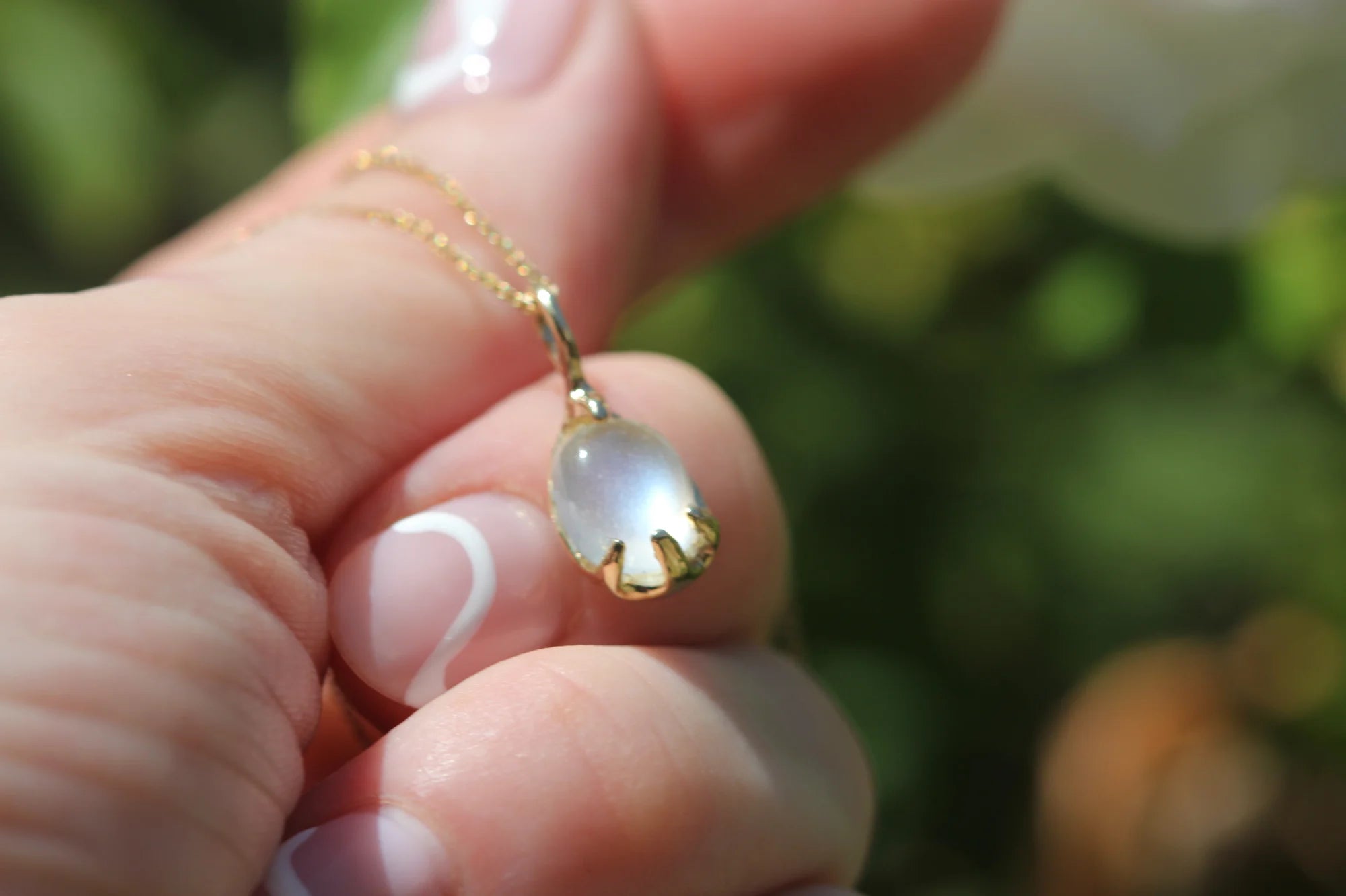 Gold necklace with a pendant held by a hand against a blurred green background
