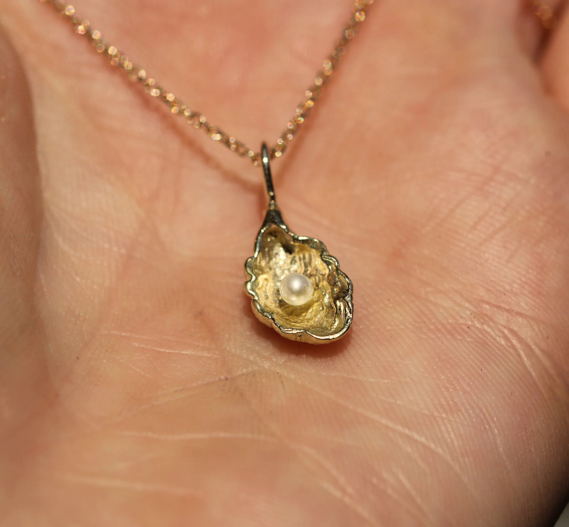 Gold pendant with a pearl on a chain held against skin