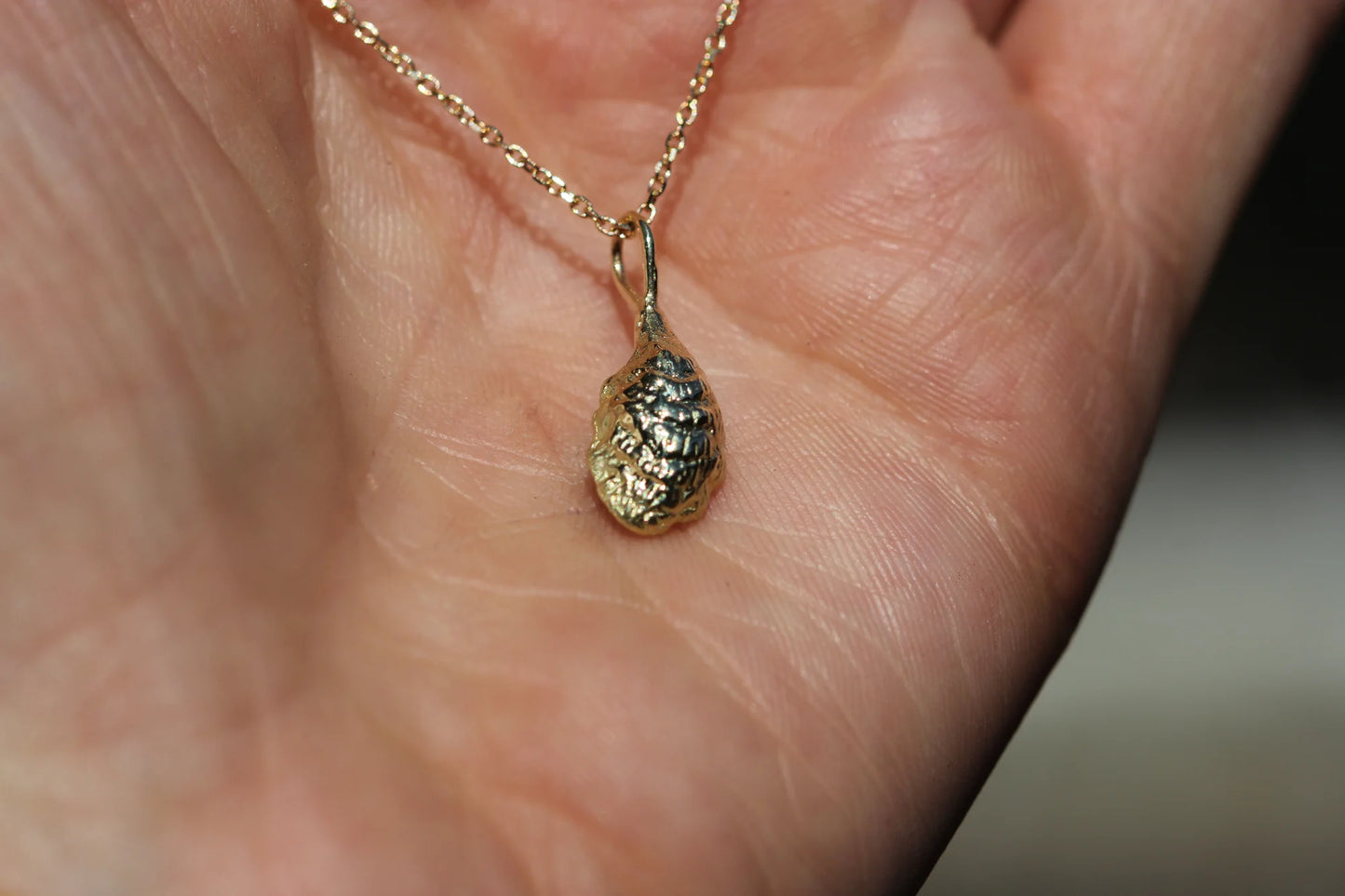Gold necklace with a small pendant held in a hand against a blurred background
